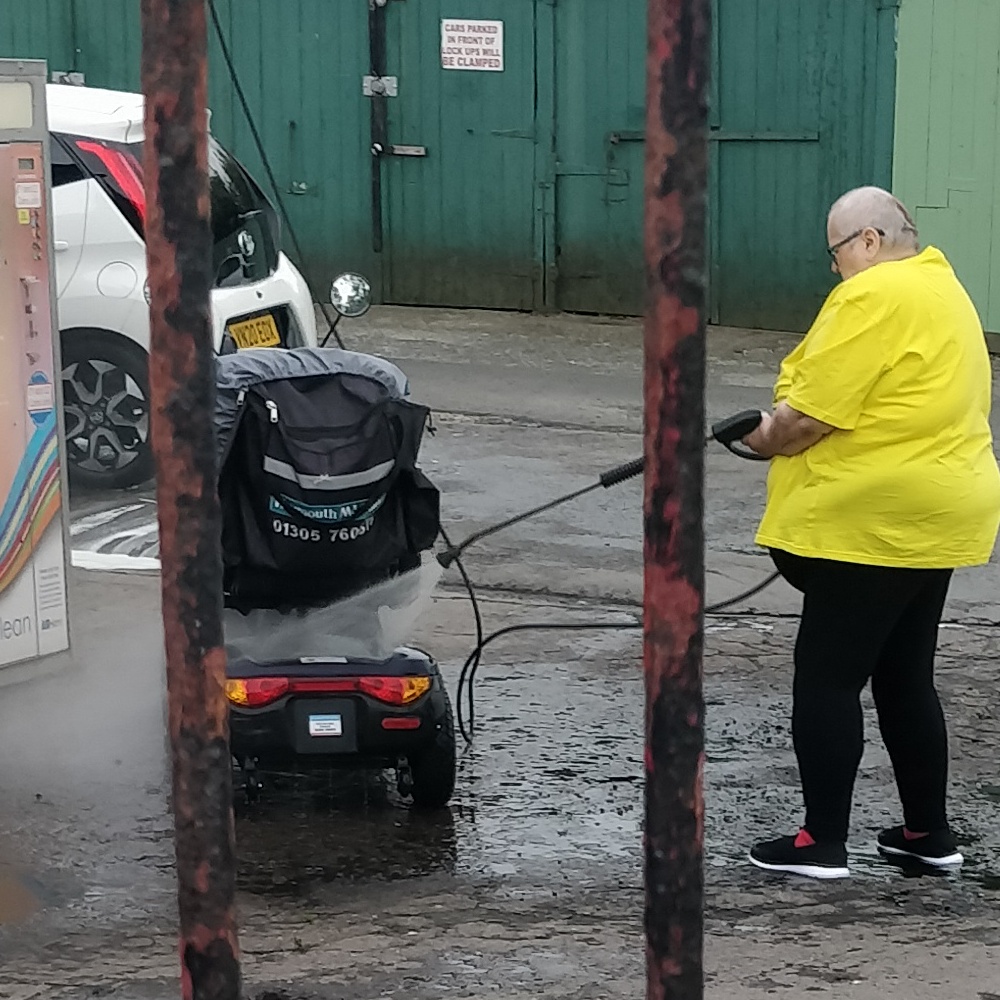 A large person powerhosing a mobility scooter - July 2022